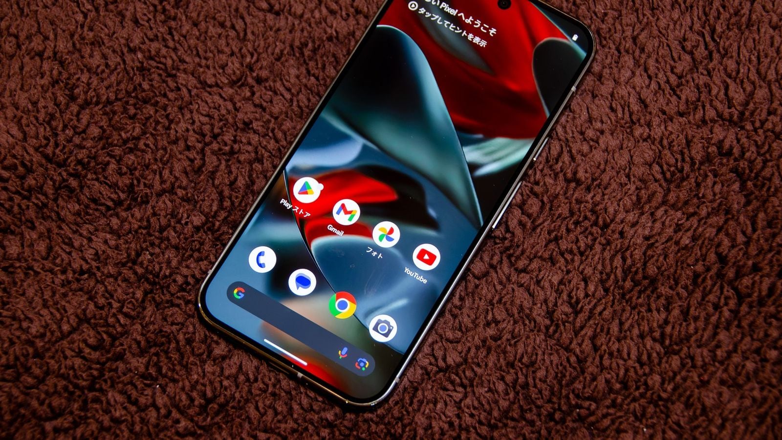 Google Pixel telefon na textilním podkladu se zobrazenou domovskou obrazovkou Androidu a ikonami aplikací